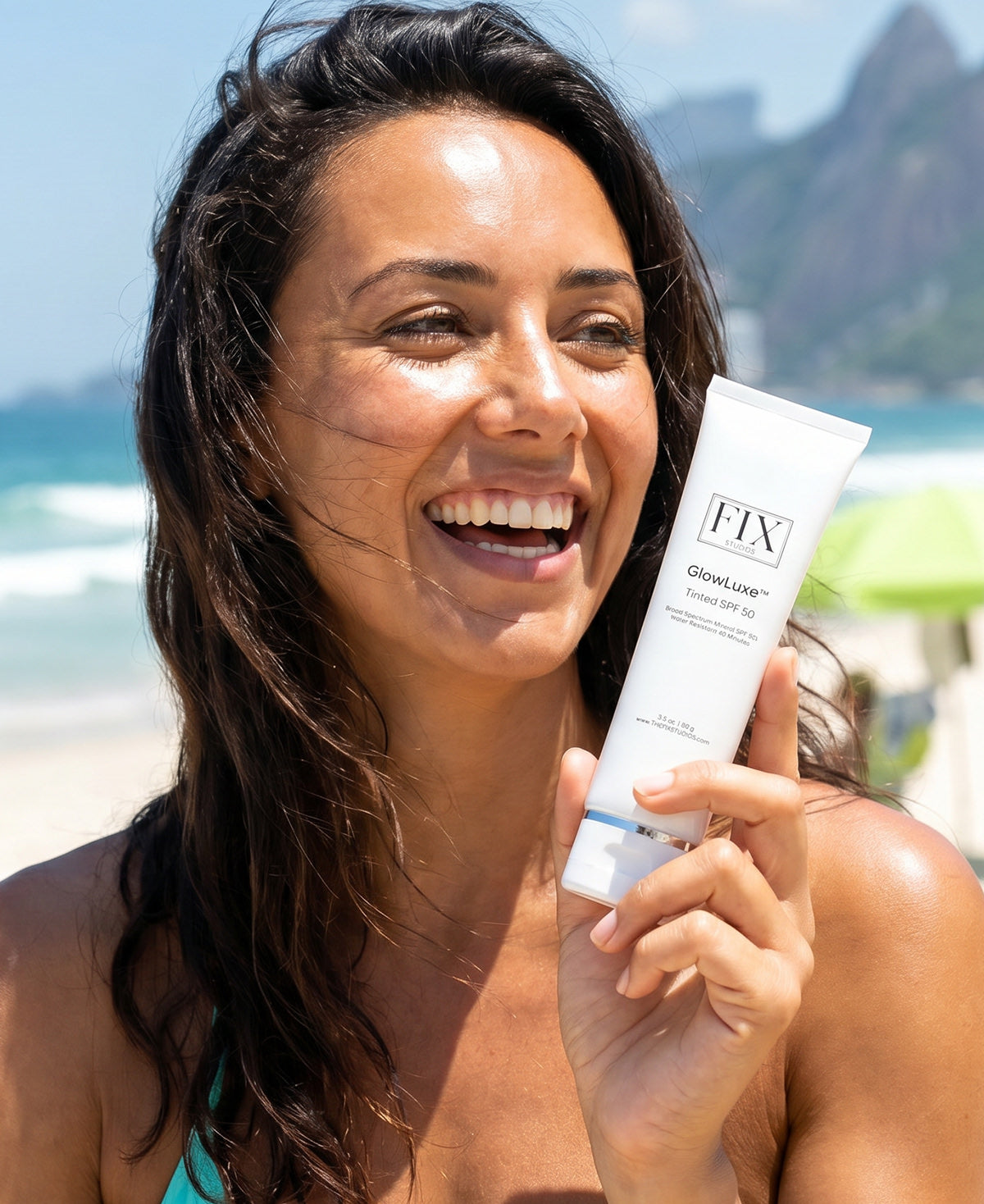 Close of up a beautiful woman holding a bottle of Fix Studios medical-grade GlowLuxe™ Tinted SPF 50 sunscreen while on the beach