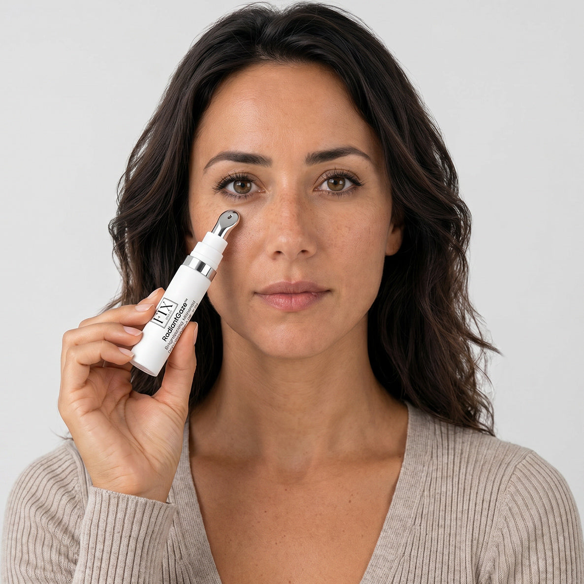 A woman holds Fix Studios medical-grade RadiantGaze™ Brightening Mineral Eye Defense SPF 50+ to her eye