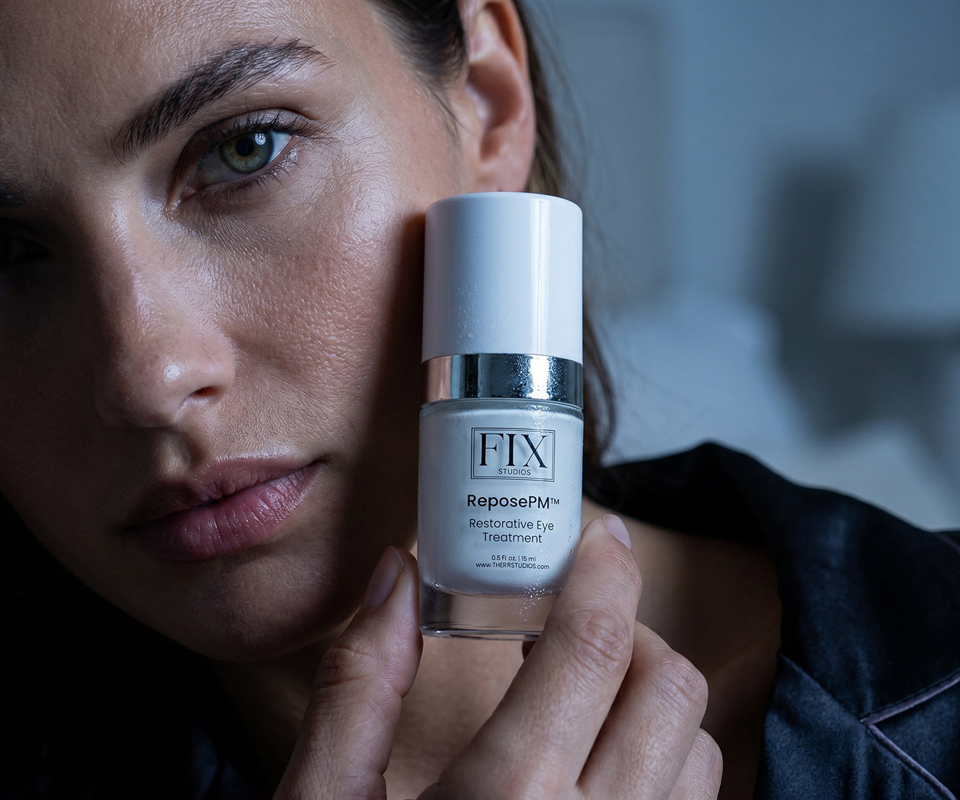 A woman holds close to her face a bottle of Fix Studios Medical-Grade ReposePM™ Restorative Eye Treatment 
